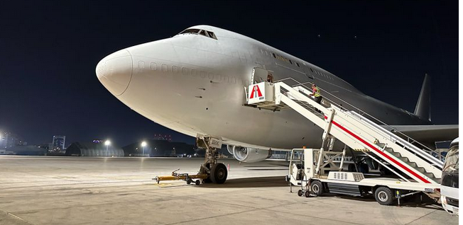Boeing 747 sur le tarmac de nuit près d’une passerelle d’embarquement